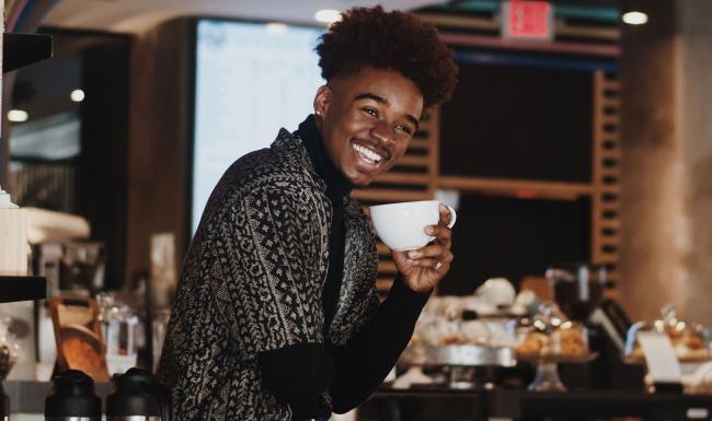 young man smiles while holding a cup of coffee in coffee shop